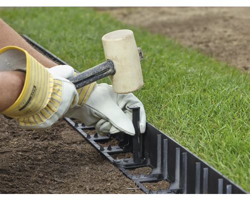 Eine Person befestigt mit einem Gummihammer eine Rasenkante.