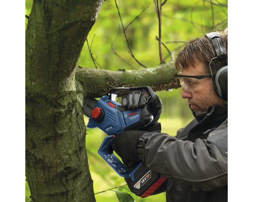 Ein Mann schneidet mit einer Akku-Kettensäge einen Ast.