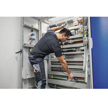 Elektriker bei der Arbeit an einem Verteilerkasten mit elektrischen Komponenten, Kabeln und Verdrahtung.