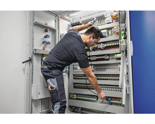 Elektriker bei der Arbeit an einem Verteilerkasten mit elektrischen Komponenten, Kabeln und Verdrahtung.