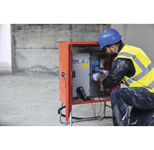 Elektriker arbeitet an einer Stromverteilerstation auf einer Baustelle.