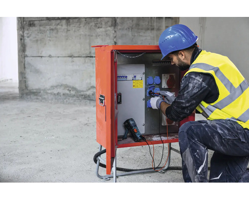 Elektriker arbeitet an einer Stromverteilerstation auf einer Baustelle.