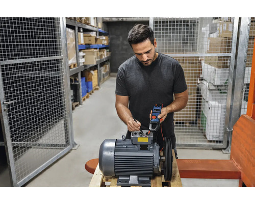 Elektriker prüft einen Elektromotor mit einem Strommessgerät in einem Lager