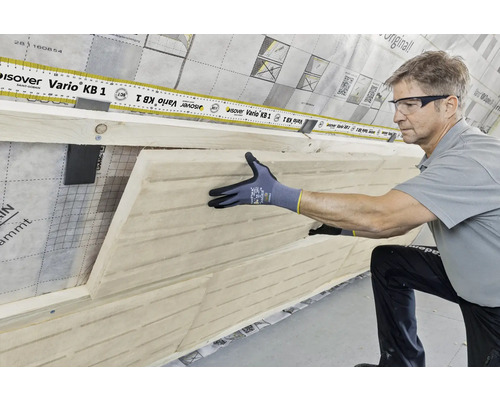 Ein Mann installiert eine Holzfaserdämmplatte mit einer Dampfbremsfolie im Innenraum.