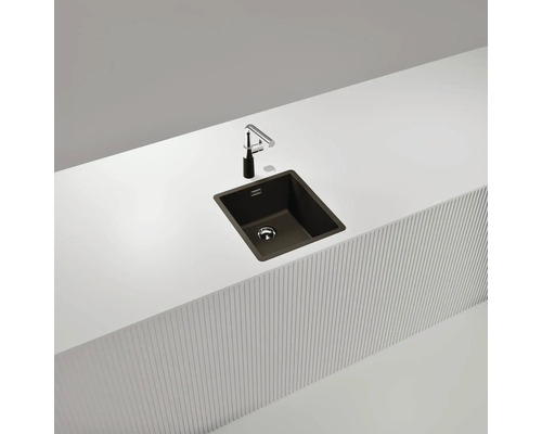 Dunkles Küchenspülbecken mit Wasserhahn auf einer weißen Arbeitsplatte.