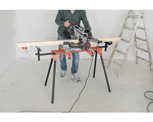 Eine Person bedient eine Kappsäge auf einem Sägetisch, neben einer Leiter.