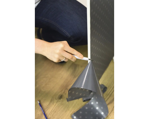 Eine Person schneidet Tapete mit einem Cuttermesser ab.