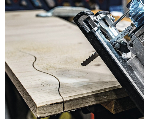 Nahaufnahme einer Stichsäge, die ein geschwungenes Muster in ein Holzbrett schneidet