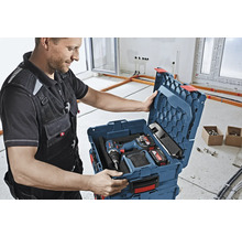 Handwerker öffnet Werkzeugkoffer mit Akkuschrauber und Akkus in einem hellen Raum.
