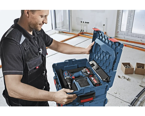 Handwerker öffnet Werkzeugkoffer mit Akkuschrauber und Akkus in einem hellen Raum.