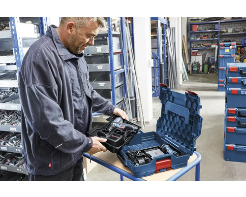 Ein Mann packt einen Akku-Bohrschrauber in einen Werkzeugkoffer, der in einem Lagerraum steht.