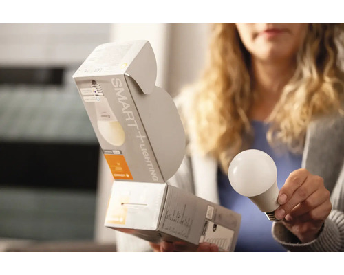 Eine Frau hält eine Smart Home Glühbirne und deren Verpackung.