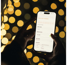Eine Person hält ein Smartphone mit einer App zur Zeitplanung für eine Steckdose in der Hand.