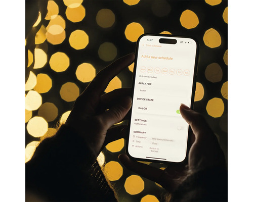 Eine Person hält ein Smartphone mit einer App zur Zeitplanung für eine Steckdose in der Hand.