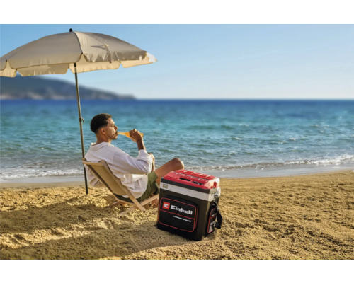 Ein Mann entspannt am Strand unter einem Sonnenschirm mit einer Einhell Kühlbox neben sich