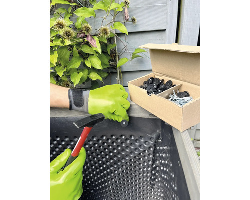 Person befestigt Noppenfolie mit Hammer und Befestigungsknöpfen in einem Pflanzkasten.