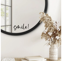Dekoratives Interieur mit rundem Spiegel, Schriftzug ''smile'', Ziergras und gemusterter Vase.
