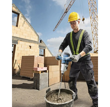 Ein Bauarbeiter mischt Mörtel mit einem elektrischen Mörtelrührer auf einer Baustelle.