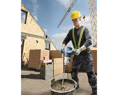 Ein Bauarbeiter mischt Mörtel mit einem elektrischen Mörtelrührer auf einer Baustelle.