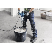 Handwerker mischt Material mit einem Mörtelrührer in einem Eimer.