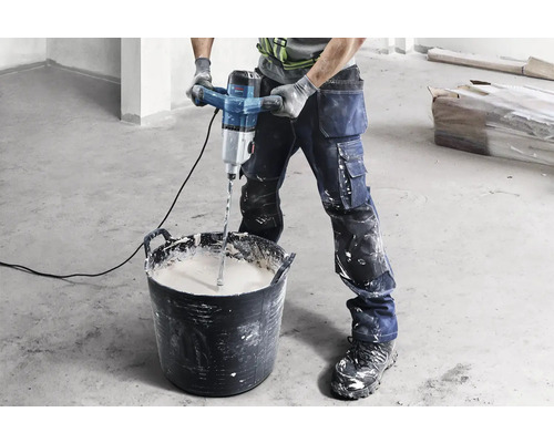 Handwerker mischt Material mit einem Mörtelrührer in einem Eimer.