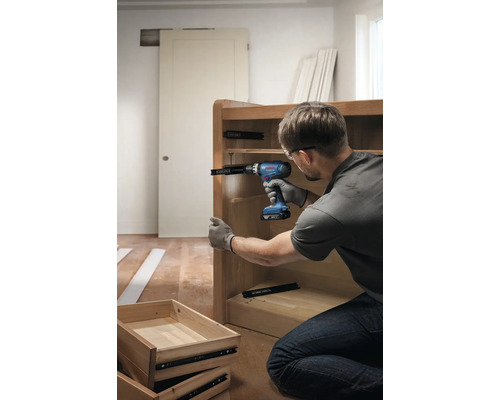 Eine Person montiert mit einem Akku-Bohrschrauber einen Schubladenauszug an einem Holzschrank.