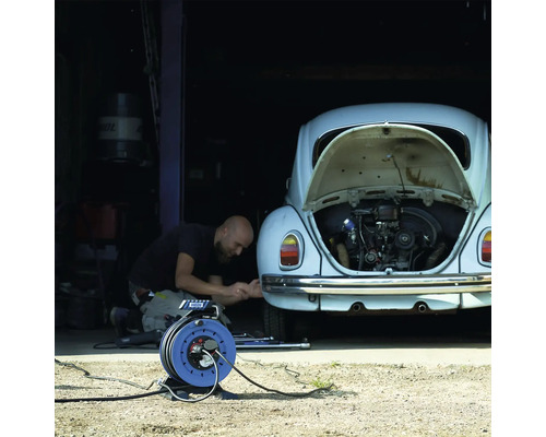 Eine Person repariert ein Auto in einer Garage mit einer Kabeltrommel.