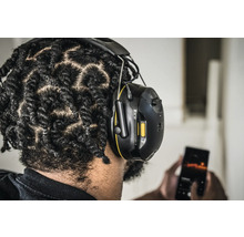 Person mit 3M Gehörschutzkopfhörern, die ein Mobiltelefon benutzt.