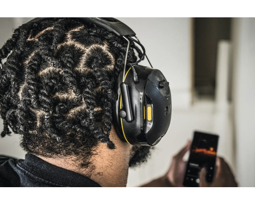 Person mit 3M Gehörschutzkopfhörern, die ein Mobiltelefon benutzt.