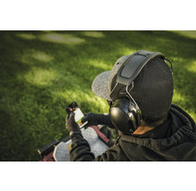Person mit Kapselgehörschutz und Smartphone im Freien