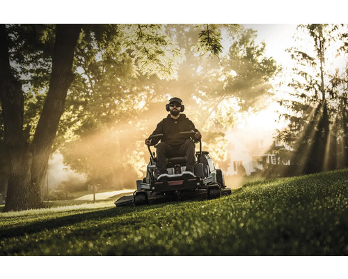 Mann mit Rasenmäher im Garten, ausgestattet mit Kopfhörern und Sonnenbrille
