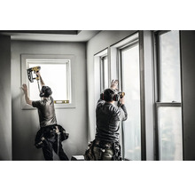 Zwei Handwerker installieren Fenster mit einem Druckluftnagler.