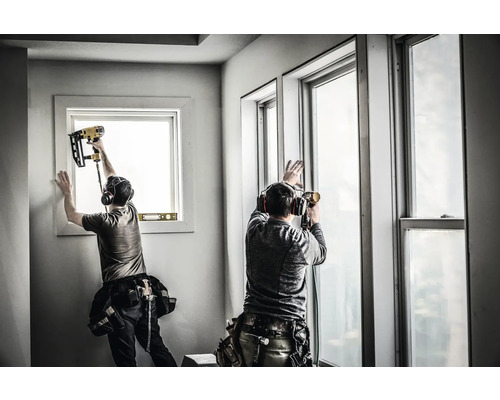 Zwei Handwerker installieren Fenster mit einem Druckluftnagler.