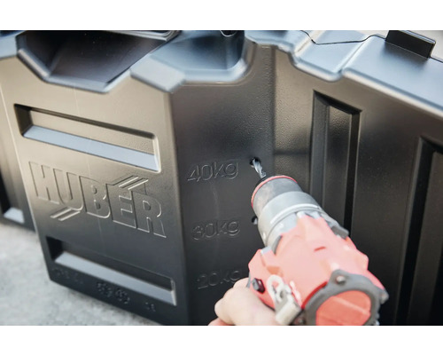 Ein Mann bohrt ein Loch in eine schwarze Huber Regentonne.