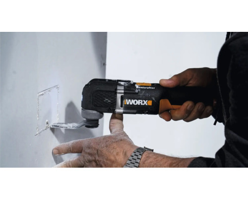 Ein Mann benutzt einen Multifunktionsschneider von Worx, um einen rechteckigen Ausschnitt in eine weiße Wand zu schneiden.