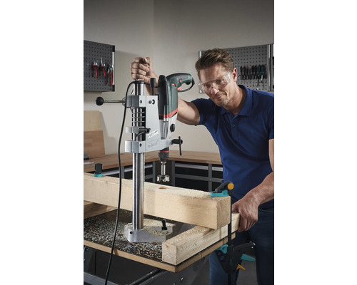 Mann bohrt mit Bohrmaschine und Bohrständer ein Loch in ein Holzbrett.