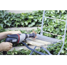 Handwerker beim Abschleifen eines Holzstuhls mit einer Bohrmaschine und Schleifaufsatz im Außenbereich.