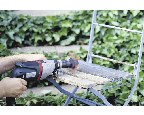 Handwerker beim Abschleifen eines Holzstuhls mit einer Bohrmaschine und Schleifaufsatz im Außenbereich.