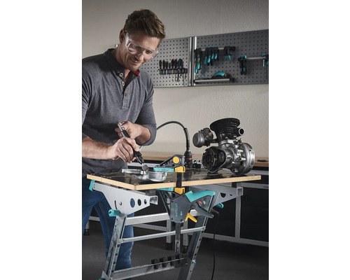 Mann mit Schutzbrille bearbeitet Metallteil auf einer Wolfcraft Werkbank mit einem Multifunktionswerkzeug.