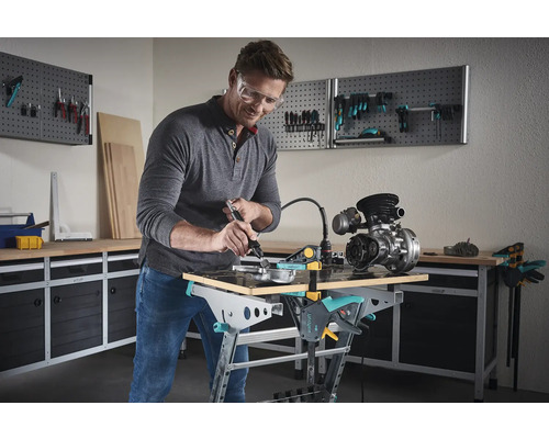 Mann arbeitet mit einem Multifunktionswerkzeug an einem Werkstück auf einer Wolfcraft Werkbank in einer Werkstatt.