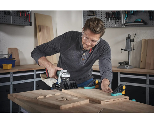 Ein Mann benutzt eine Nutfräse an Holzbrettern in einer Werkstatt.