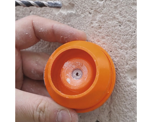 Nahaufnahme einer Person, die mit einem Bohrer und einem orangenen Staubschutz arbeitet