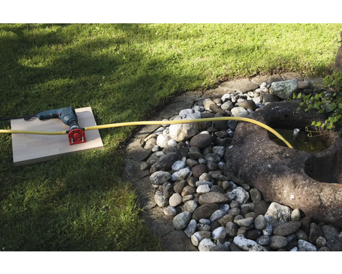 Eine Bohrmaschine mit Wasseranschluss und Schlauch im Garten.