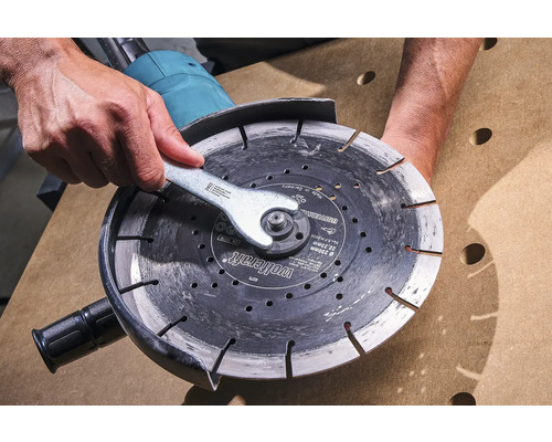 Person wechselt Trennscheibe mit Schraubenschlüssel an einem Winkelschleifer