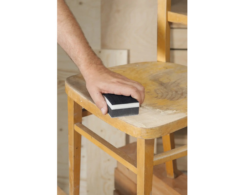 Eine Person schleift einen Holzstuhl mit einem Schleifklotz