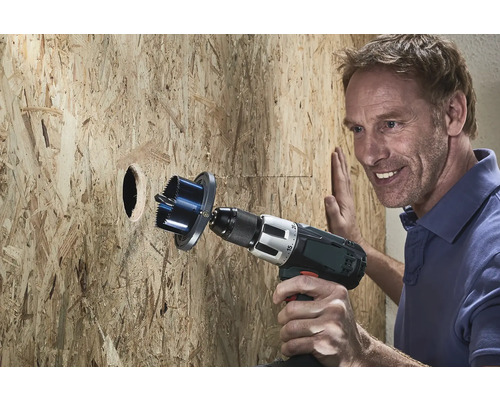 Mann bohrt mit einer Lochsäge ein Loch in eine Holzwand.