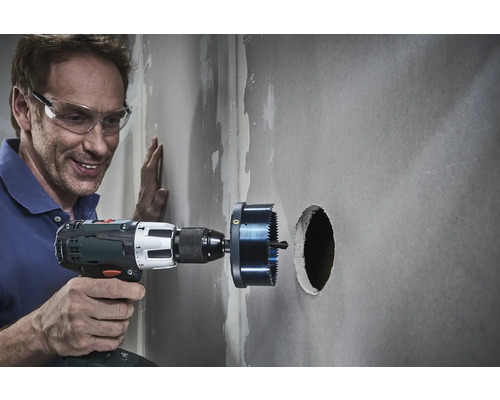 Handwerker bohrt mit einer Lochsäge ein Loch in eine Wand