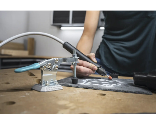 Arbeitstischszene mit Graviergerät, Schraubzwinge und bearbeiteter Schieferplatte