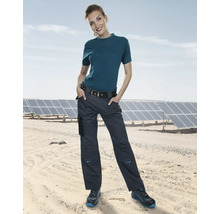 Frau trägt eine Arbeitshose und ein T-Shirt vor Solarmodulen.