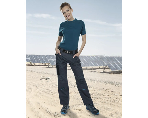 Frau trägt eine Arbeitshose und ein T-Shirt vor Solarmodulen.